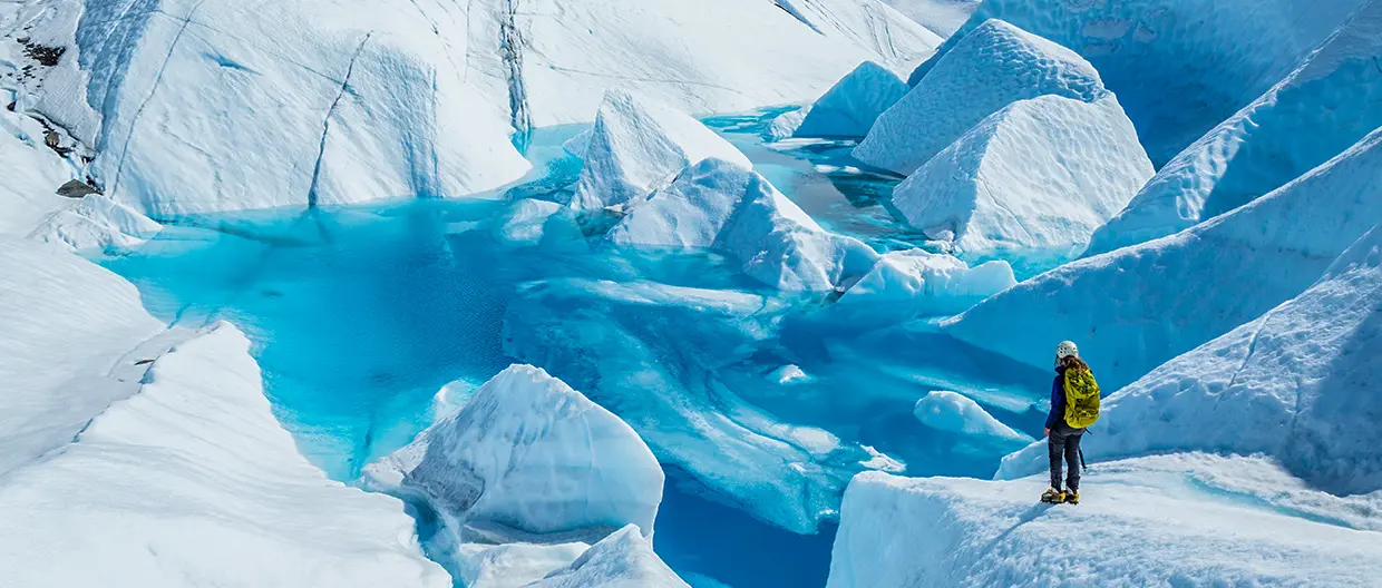 A woman watching a pool of water in a huge glacier