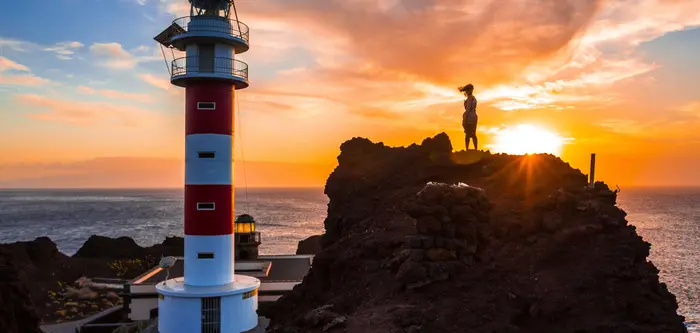 A female tourist admiring a lighthouse in the sunset