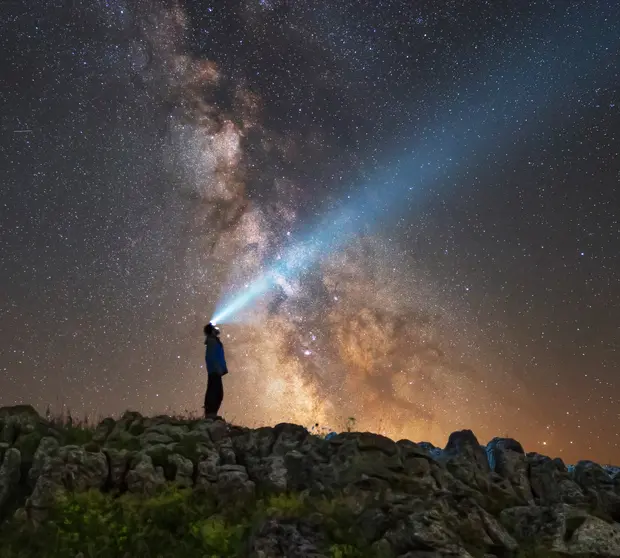 Man looking up a starry sky with a torchlight