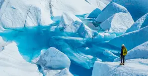 A woman watching a pool of water in a huge glacier