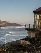 foto di un faro sul mare con scogliera in lontananza