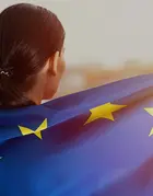 A woman wrapped in the EU flag watching the sunset.