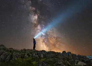 Man looking up a starry sky with a torchlight