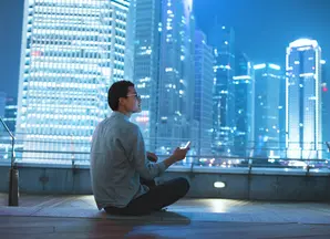 A man holding a smartphone and watching the skyscrapers around him.
