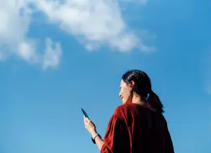 Frau mit Telefon vor blauem Himmel