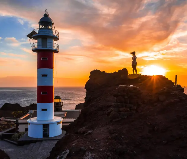 A female tourist admiring a lighthouse in the sunset