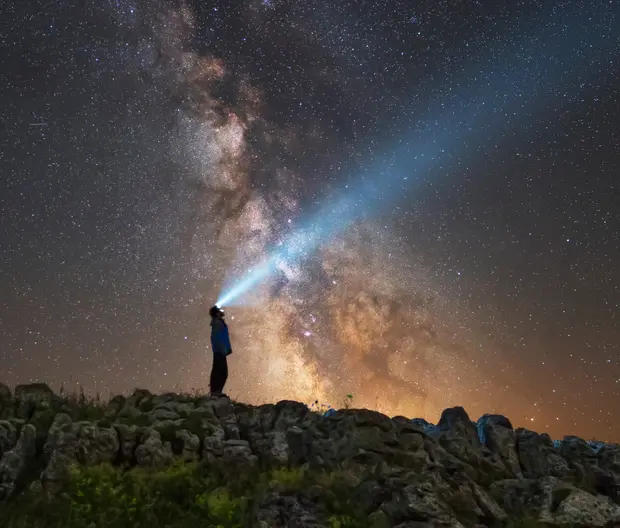 Man looking up a starry sky with a torchlight