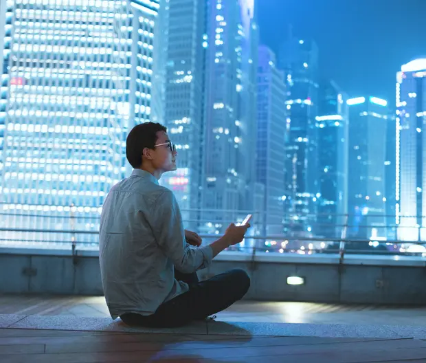 A man holding a smartphone and watching the skyscrapers around him.