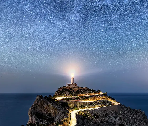 foto di un faro su una scogliera e di un cielo stellato