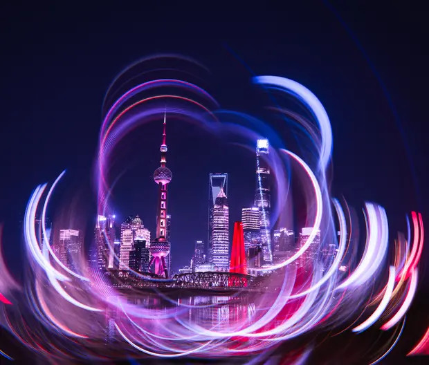 A dynamic, long-exposure photograph of the Shanghai skyline, featuring the Oriental Pearl Tower and other skyscrapers, taken using a camera rotation technique.