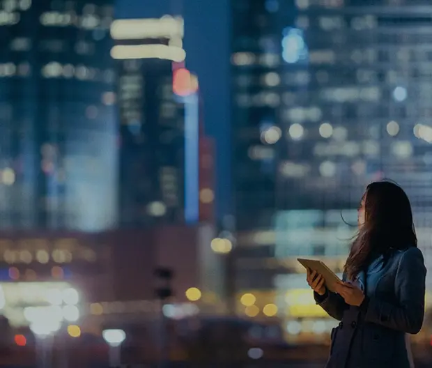 immagine di una ragazza con un tablet in mano su sfondo skyline notturno