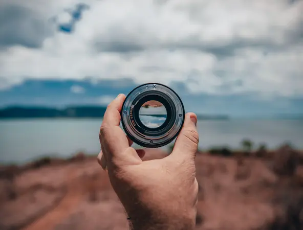 A hand holding a camera lens against a blurred background in the distance