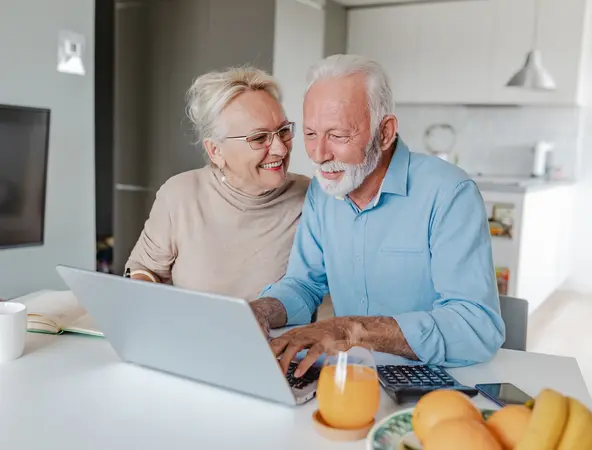 Glückliches, älteres Paar sitzt beim Laptop