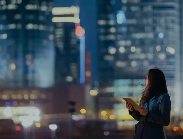 immagine di una ragazza con un tablet in mano su sfondo skyline notturno