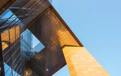 Bâtiment moderne en verre et métal, reflétant un ciel bleu dans un environnement financier.