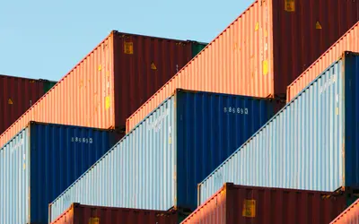 Conteneurs empilés sous un ciel bleu, symbolisant le commerce et la logistique financière.