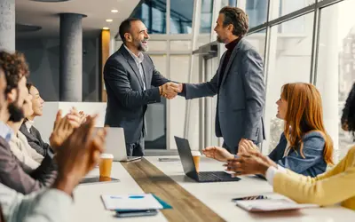 Deux professionnels se serrent la main dans les bureaux d'Amundi, applaudis par des collègues.
