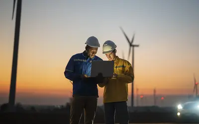 Deux experts en énergie renouvelable examinent des données sur un ordinateur portable au coucher de soleil.
