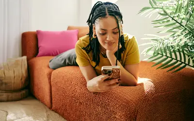 Femme concentrée sur son téléphone dans un cadre décontracté, symbolisant la gestion financière.