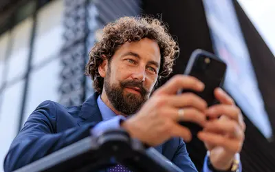 Un homme consulte son téléphone devant un bâtiment moderne.