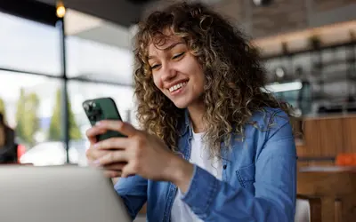 Femme utilisant un smartphone et un ordinateur portable dans un café.