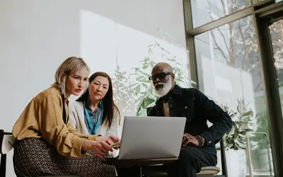 Trois collaborateurs, deux femmes et un homme regardent un ordinateur.