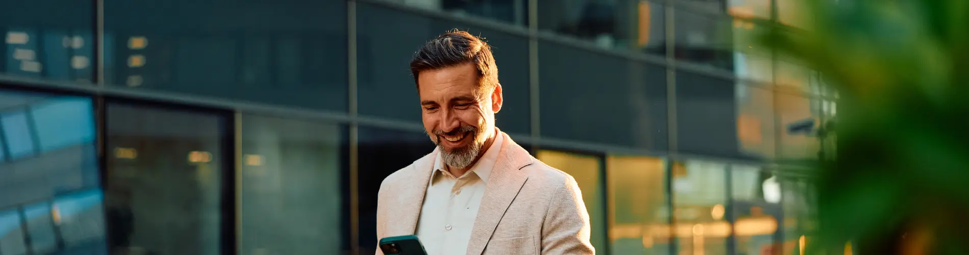 Gestionnaire d'actifs souriant vérifiant son téléphone devant des bureaux d'Amundi.