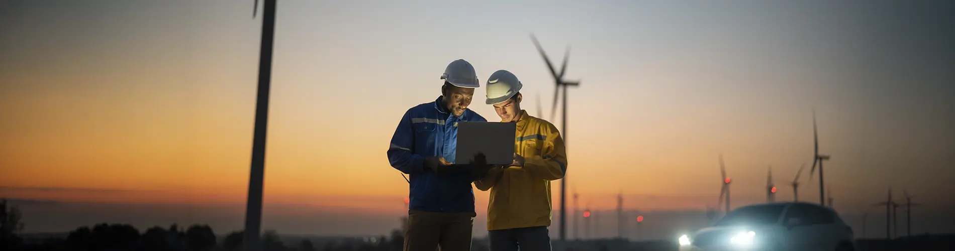 Deux experts en énergie renouvelable examinent des données sur un ordinateur portable au coucher de soleil.