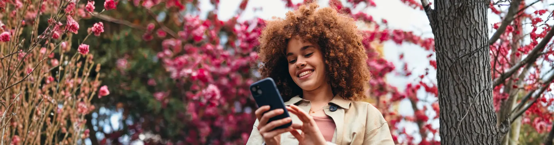 Femme souriante, utilisante son téléphone, entourée de fleurs à Amundi.