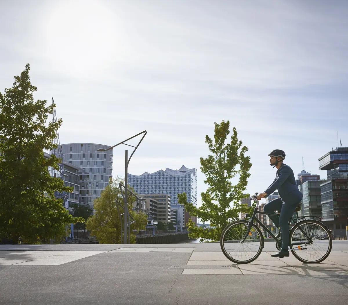 Un gestionnaire d'actifs à vélo, avec des bâtiments modernes en arrière-plan au soleil.