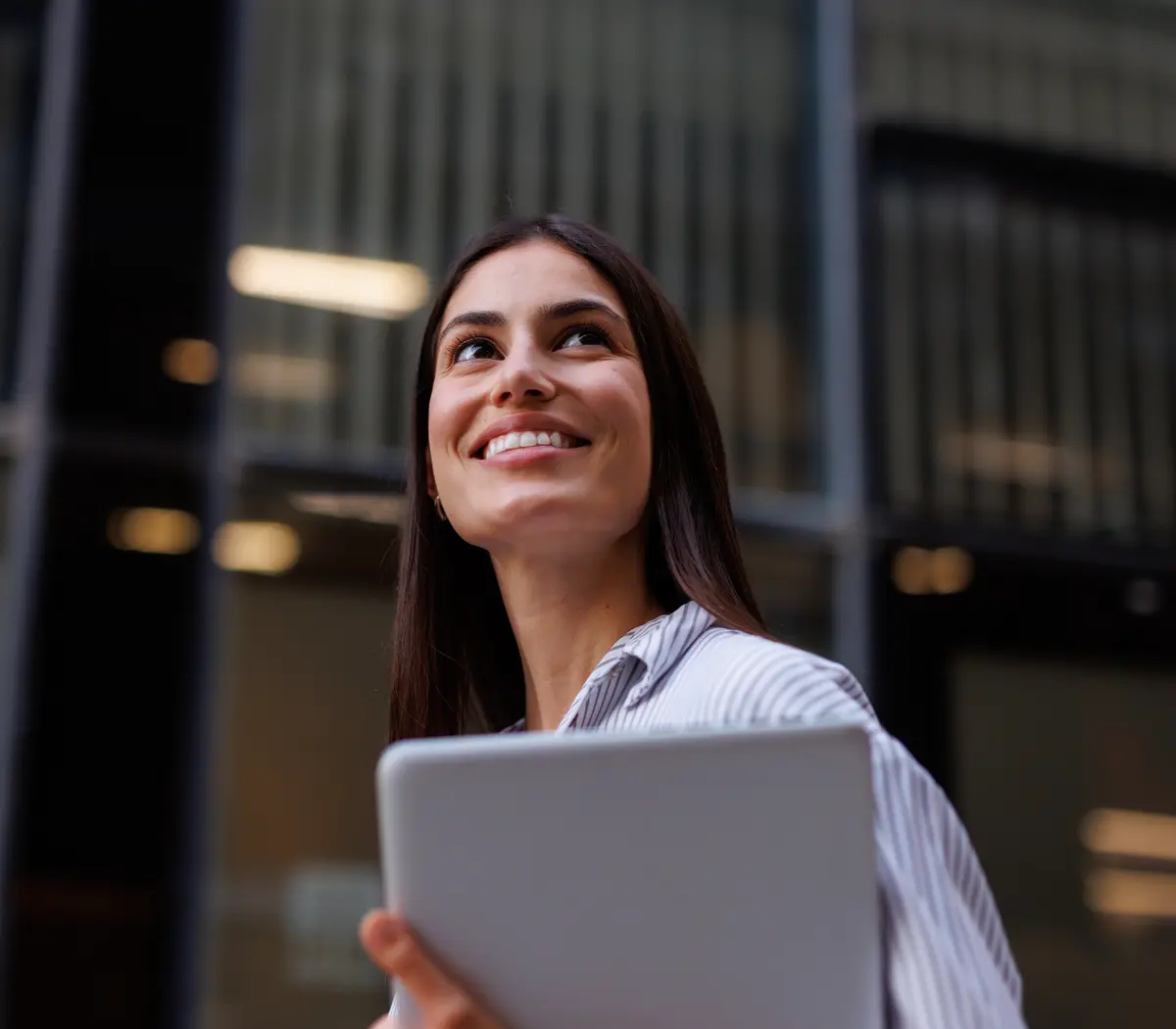 Salariée d'une entreprise qui regarde vers le ciel avec une tablette dans les mains.