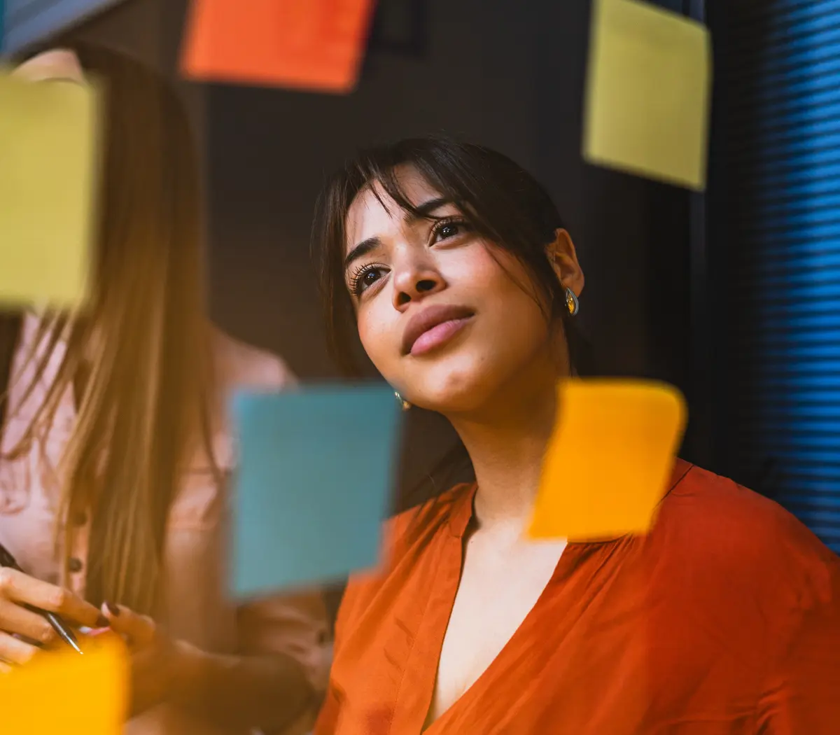 Femme qui regarde un mur de post-its colorés.