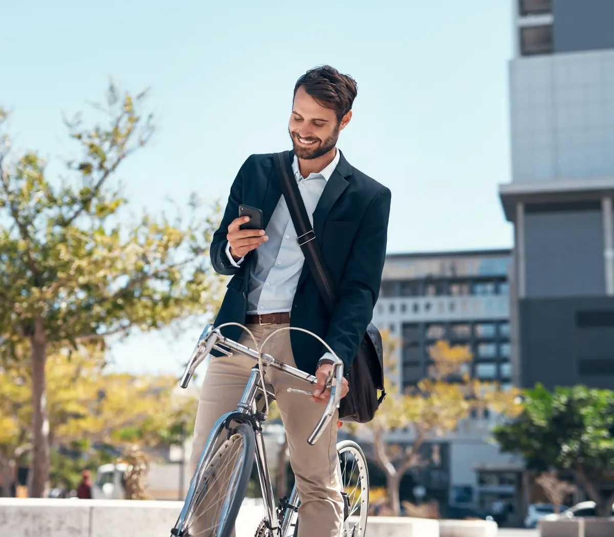Un gestionnaire d'actifs souriant consulte son téléphone à côté de son vélo en milieu urbain.
