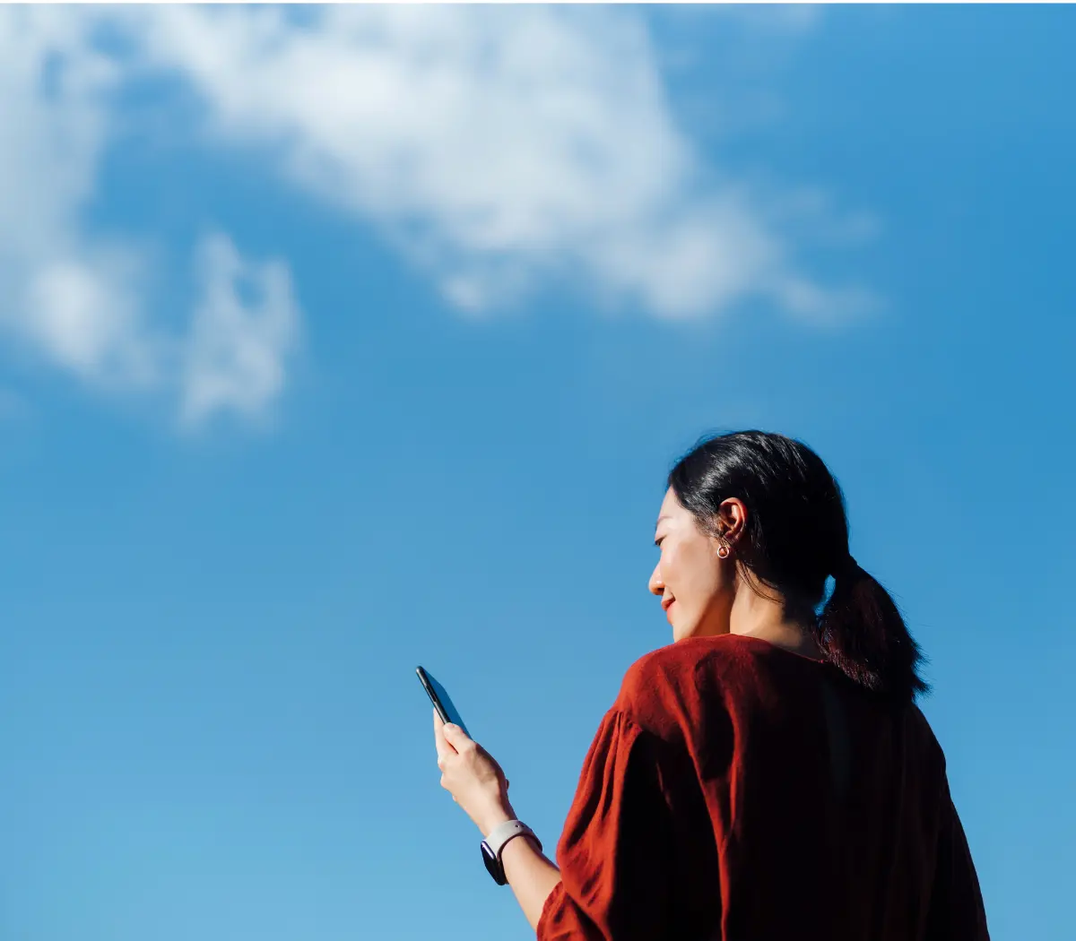 Femme utilisant son téléphone, sous un ciel bleu clair.