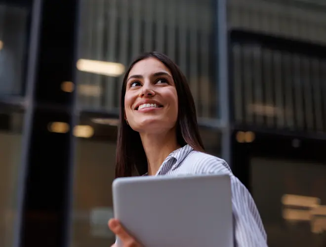 Salariée d'une entreprise qui regarde vers le ciel avec une tablette dans les mains.