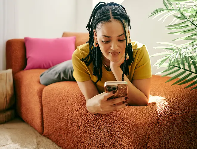 Femme concentrée sur son téléphone dans un cadre décontracté, symbolisant la gestion financière.