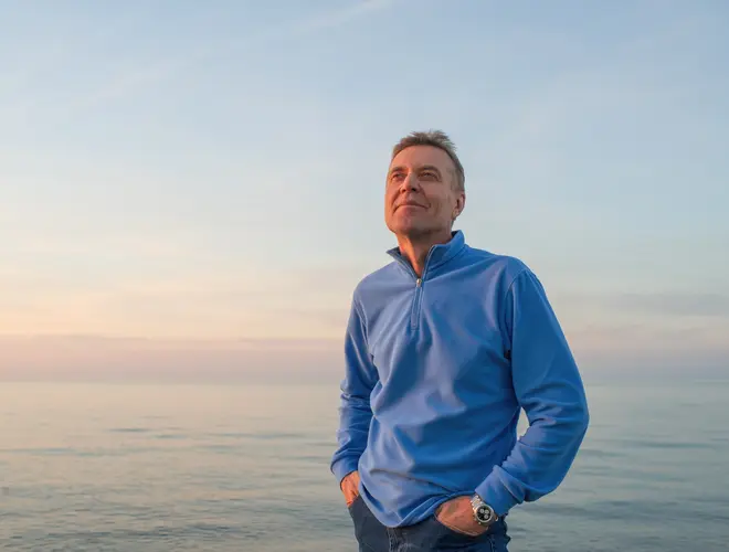 Homme souriant en bord de mer, représentant un futur retraité.