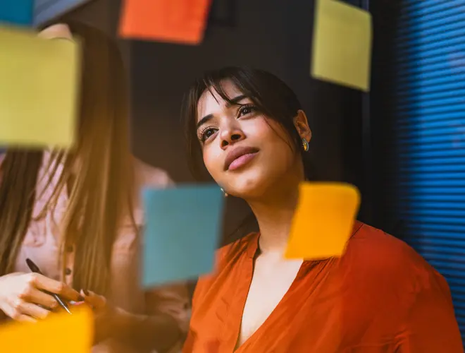 Femme qui regarde un mur de post-its colorés.