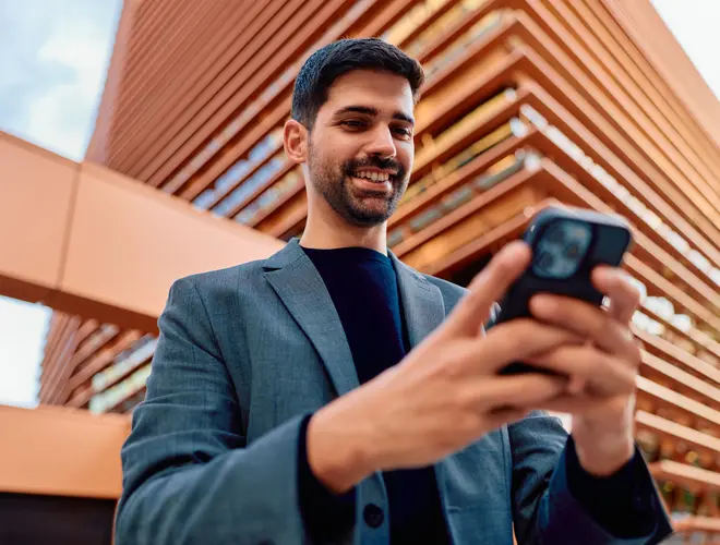 Un salarié consulte son téléphone devant un bâtiment moderne .