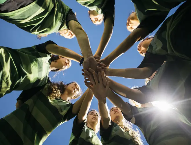 Des jeunes sportives regroupent leurs mains en cercle, symbolisant la collaboration et l'esprit d'équipe.