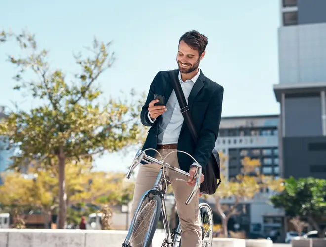 Un gestionnaire d'actifs souriant consulte son téléphone à côté de son vélo en milieu urbain.