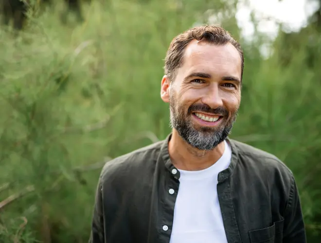Un expert financier souriant dans un environnement naturel, vêtu décontracté.