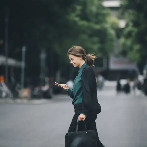 Femme en costume traversant une rue, consultant son téléphone, cadre professionnel.
