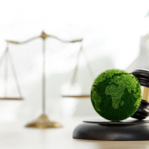 Un globe vert sur un maillet de juge, symbole d'une gestion financière durable. Balance en arrière-plan.