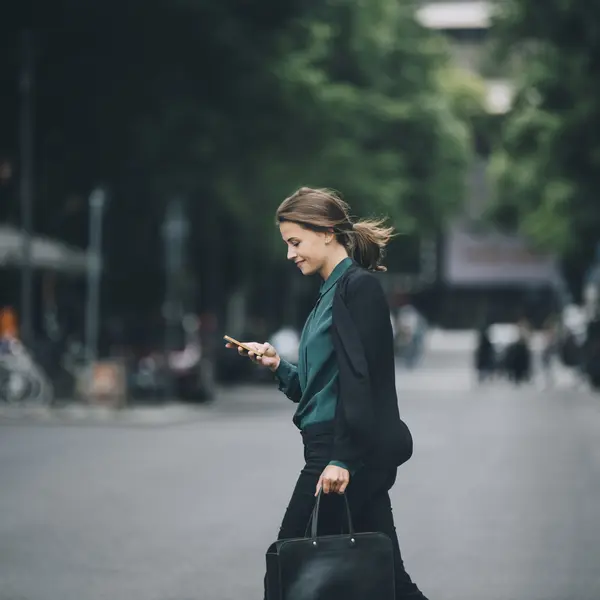 Femme en costume traversant une rue, consultant son téléphone, cadre professionnel.