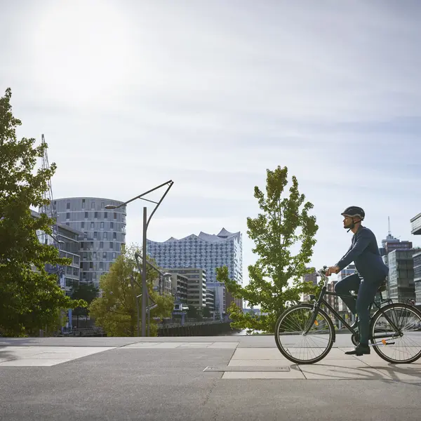 Un gestionnaire d'actifs à vélo, avec des bâtiments modernes en arrière-plan au soleil.