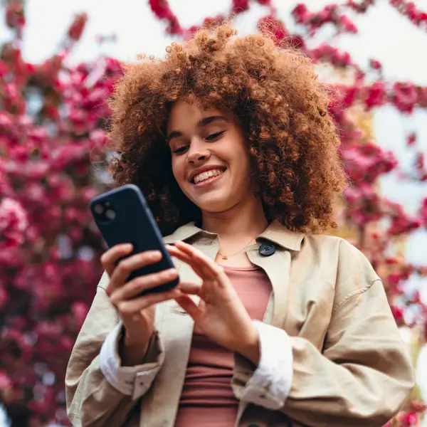 Femme consultant son téléphone avec des fleurs de printemps en arrière-plan.