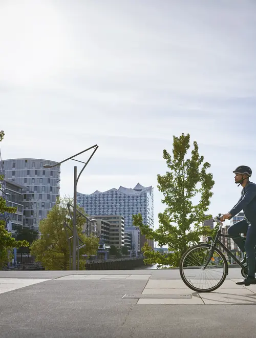 Un gestionnaire d'actifs à vélo, avec des bâtiments modernes en arrière-plan au soleil.