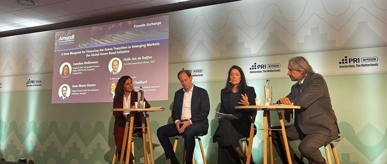 Panel discussion at the PRI in-person event in Amsterdam, with four speakers seated on stools on an Amundi-branded stage. A presentation screen shows “A New Blueprint for Financing the Green Transition in Emerging Markets” and the Global Green Bond Initiative.