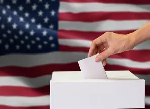 Person hält Wahlzettel, im Hintergrund die US-Flagge